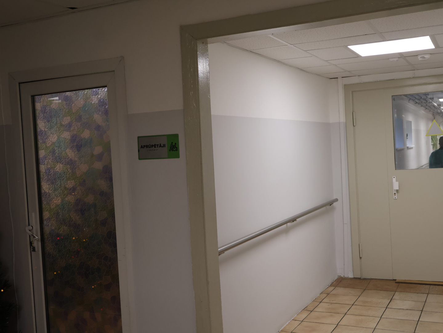 Attēlā gaitenis gaiši pelēkā krāsā ar norādes zīmi ar uzrakstu APRŪPĒTĀJI, arī braila rakstā