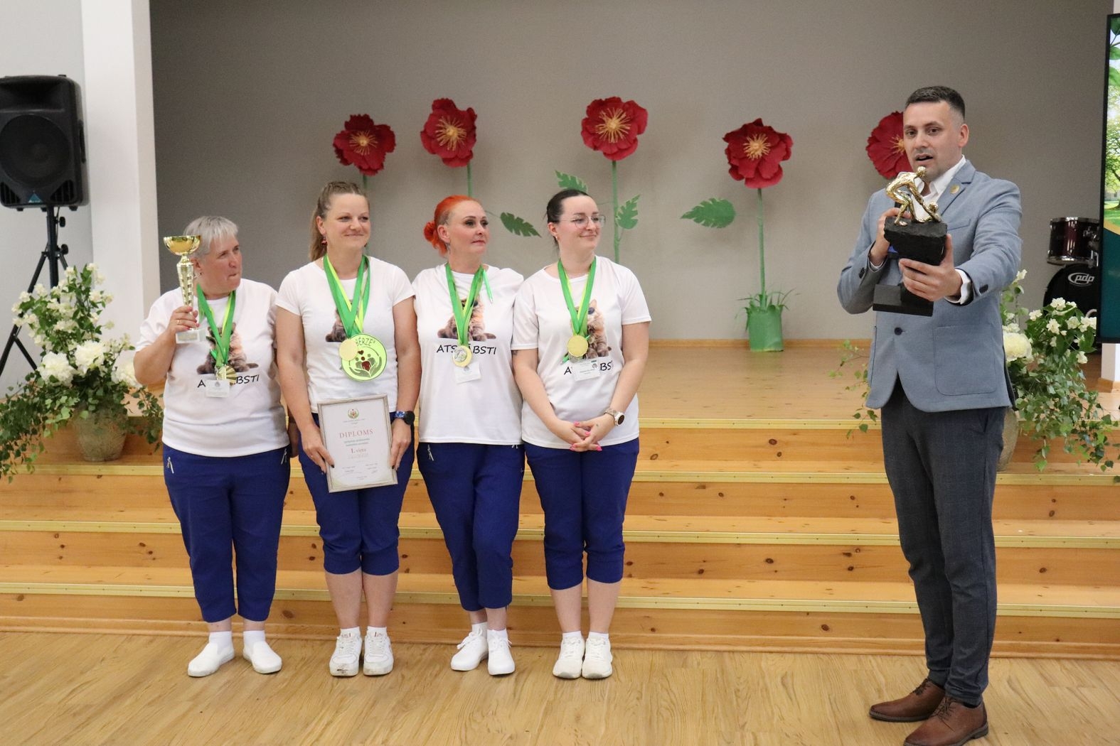 Dalībnieku komanda ar iestādes direktoru, kurš pasniedz balvu