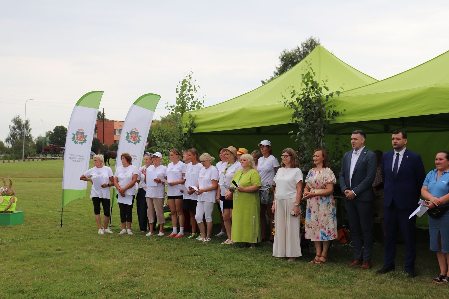 Atklāšanas pasākums, pie zaļajām teltīm un karogiem rindā stāv organizatori un vadītāji un viesi