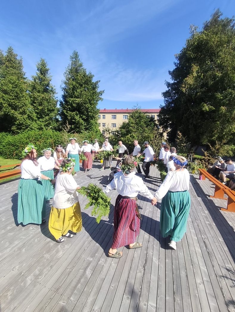 Rokās sadevušies, pasākuma dalībnieki tautastērpos un vainagos izveidojuši apli