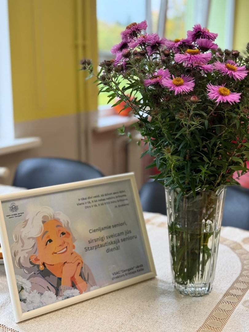 Uz galda ziedi vāzē un rāmī apsveikums senioru dienā