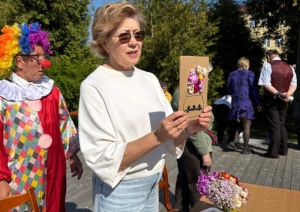 Darbiniece rāda apsveikumu kartīti veidotu izmantojot dzīvos ziedus