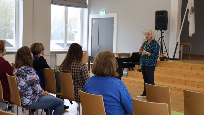 Zāles priekšā runā mākslas terapeite. Zālē sēž klausītāji