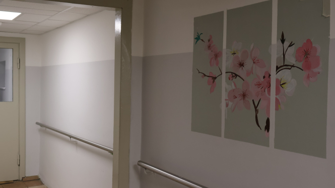 Attēlā gaitenis gaiši pelēkā krāsā ar rozā ziedu zīmējumiem uz sienas