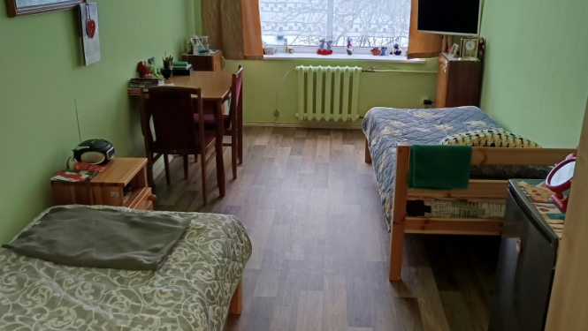 Iedzīvotāju istaba pēc remonta veikšanas, gaiši zaļas sienas, brūns grīdas segums, mēbeles