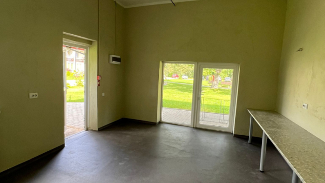 Attēls ar garāžas telpas stāvokli pēc remonta. Skaistas svaigas sienas gaišā krāsojumā, grīdas segums tumšs, gar sienu galda virsmas, plašas durvis