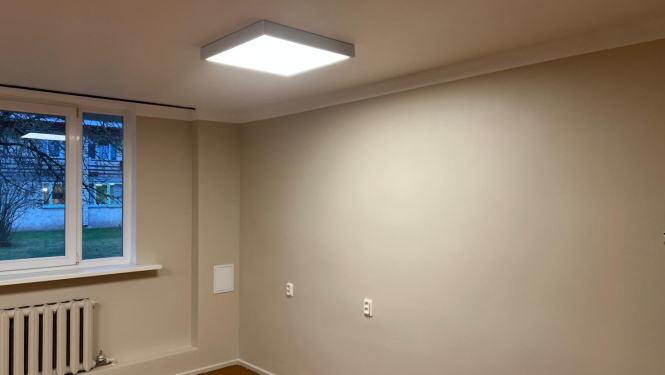 Telpa pēc remonta veikšanas. Gaišas nokrāsotas sienas bēšā krāsā. Jauna grīda, kantainas lampas pie griestiem.