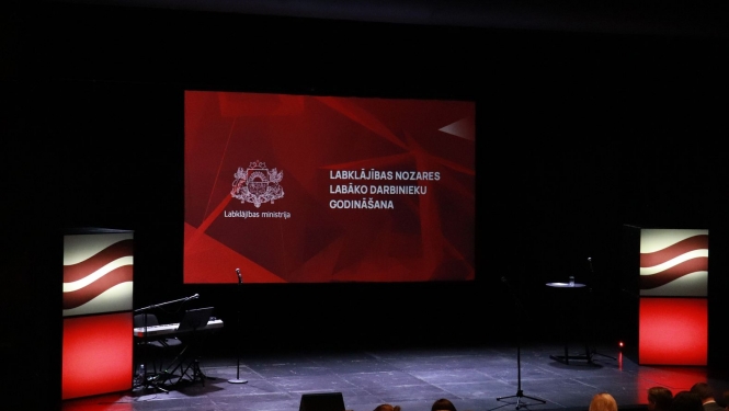 Labklājības ministrijas nozares labāko darbinieku godināšanas pasākuma skatuve. Lielais ekrāns ar ģerboni un uzrakstu "Labklājības nozares labāko darbinieku godināšana"
