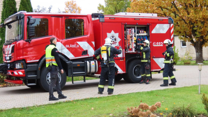 Attēlā četri ugunsdzēsēji pie ugunsdzēsēju mašīnas