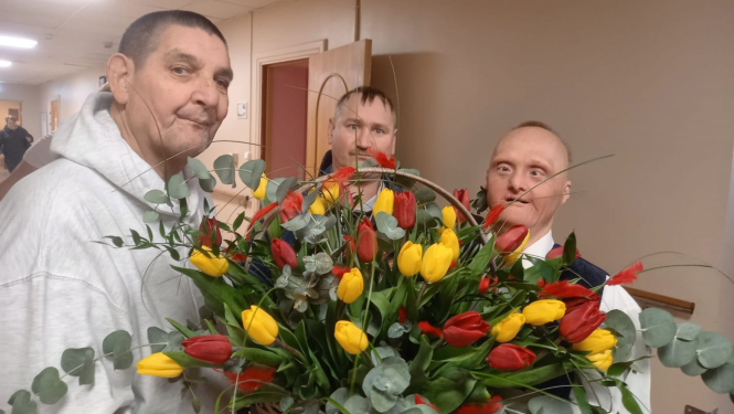 Trīs iedzīvotāji vīrieši tur grozu pilnu ar dzeltenām tulpēm