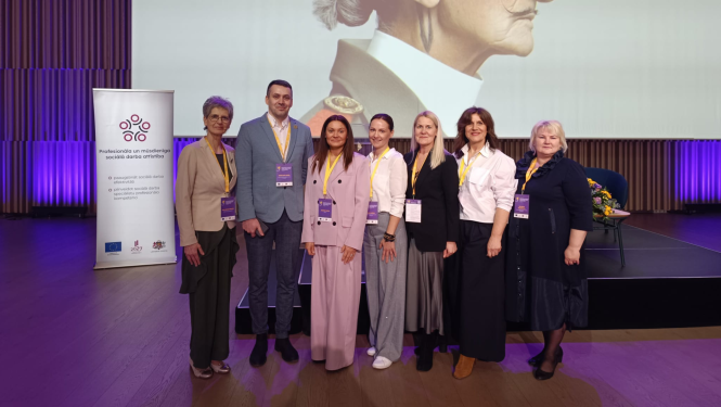 Iestādes darbinieku kopbilde. Septiņi cilvēki lietišķi ģērbušies stāv pie pasākuma skatuves.