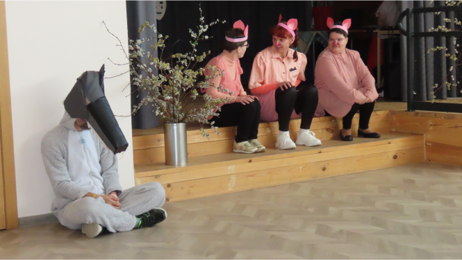 Uz skatuves sēž teātra izrādes dalībnieki tērpušies vilka un trīs sivēlu tērpos