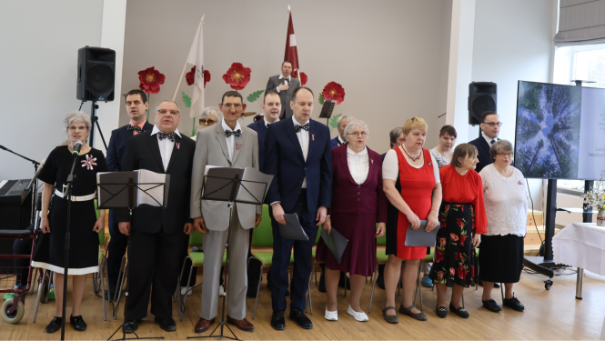 Iedzīvotāju ansamblis. Dziedātāji stāv uz skatuves un izpilda dziesmu.