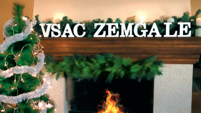 Ziemassvētku noskaņās izrotāts kamīns, kurā deg uguns, izpušķota egle. Uz kamīna malas burti VSAC ZEMGALE.