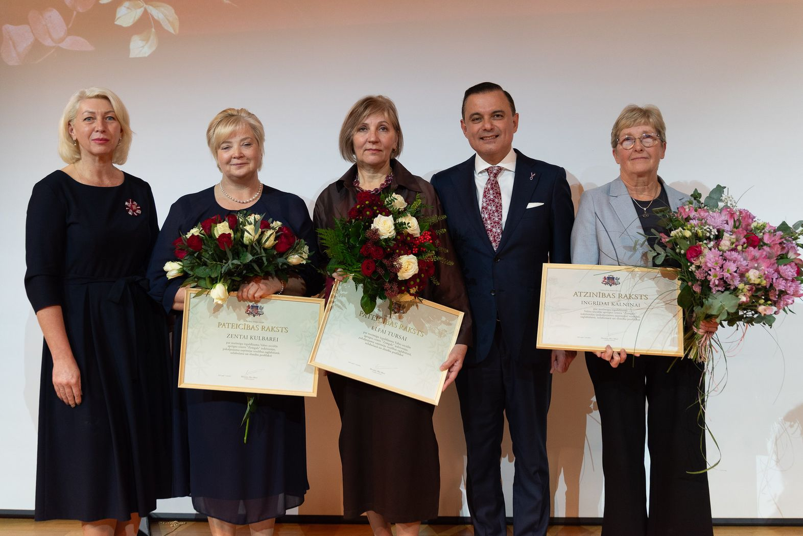 Attēlā veselības ministrs, direktora vietniece un trīs iestādes darbinieces, kuras saņēmušas ziedus un apbalvojumus