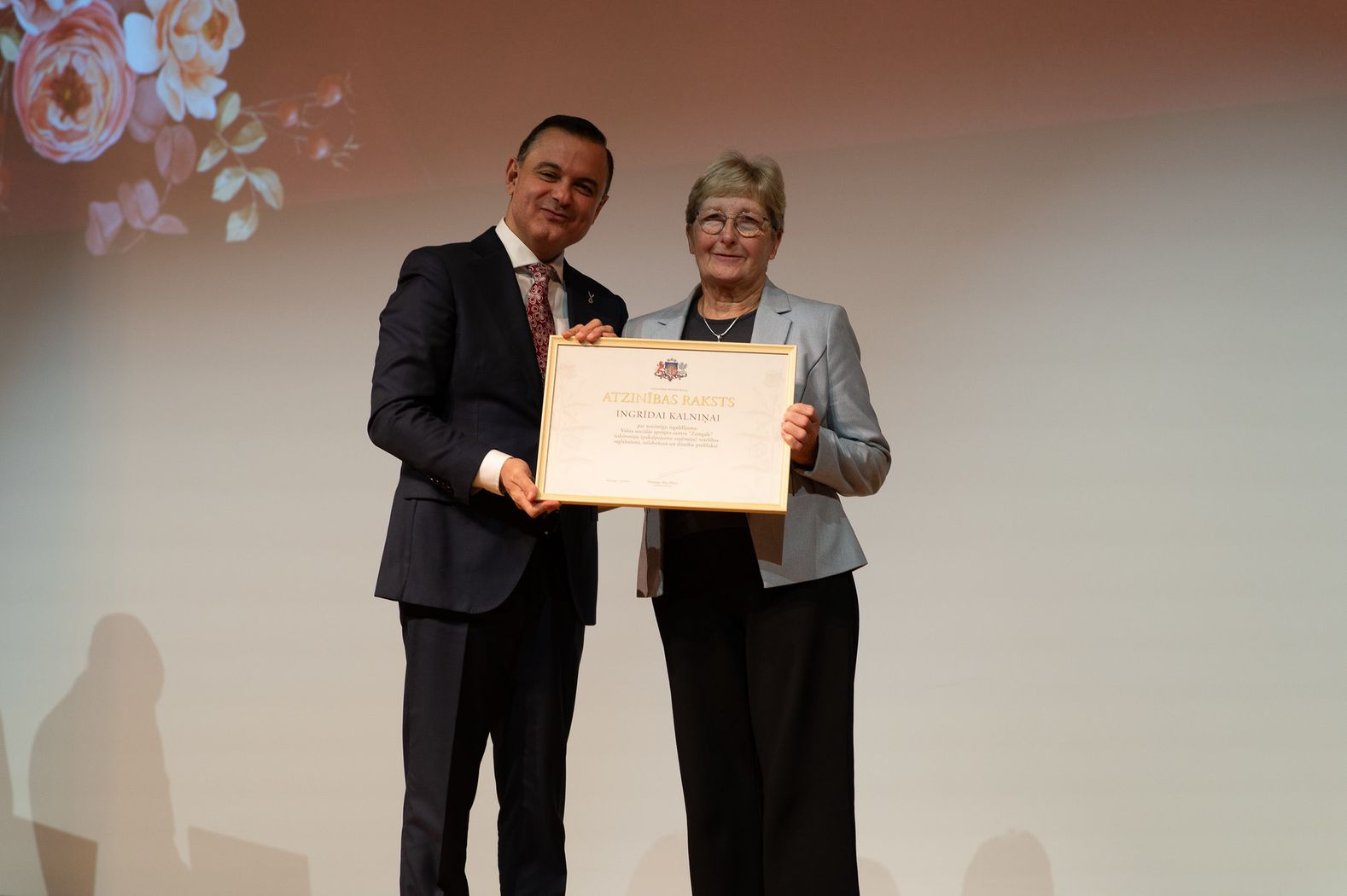 Attēlā veselības ministrs un vsac zemgale darbiniece ar saņemto apbalvojumu