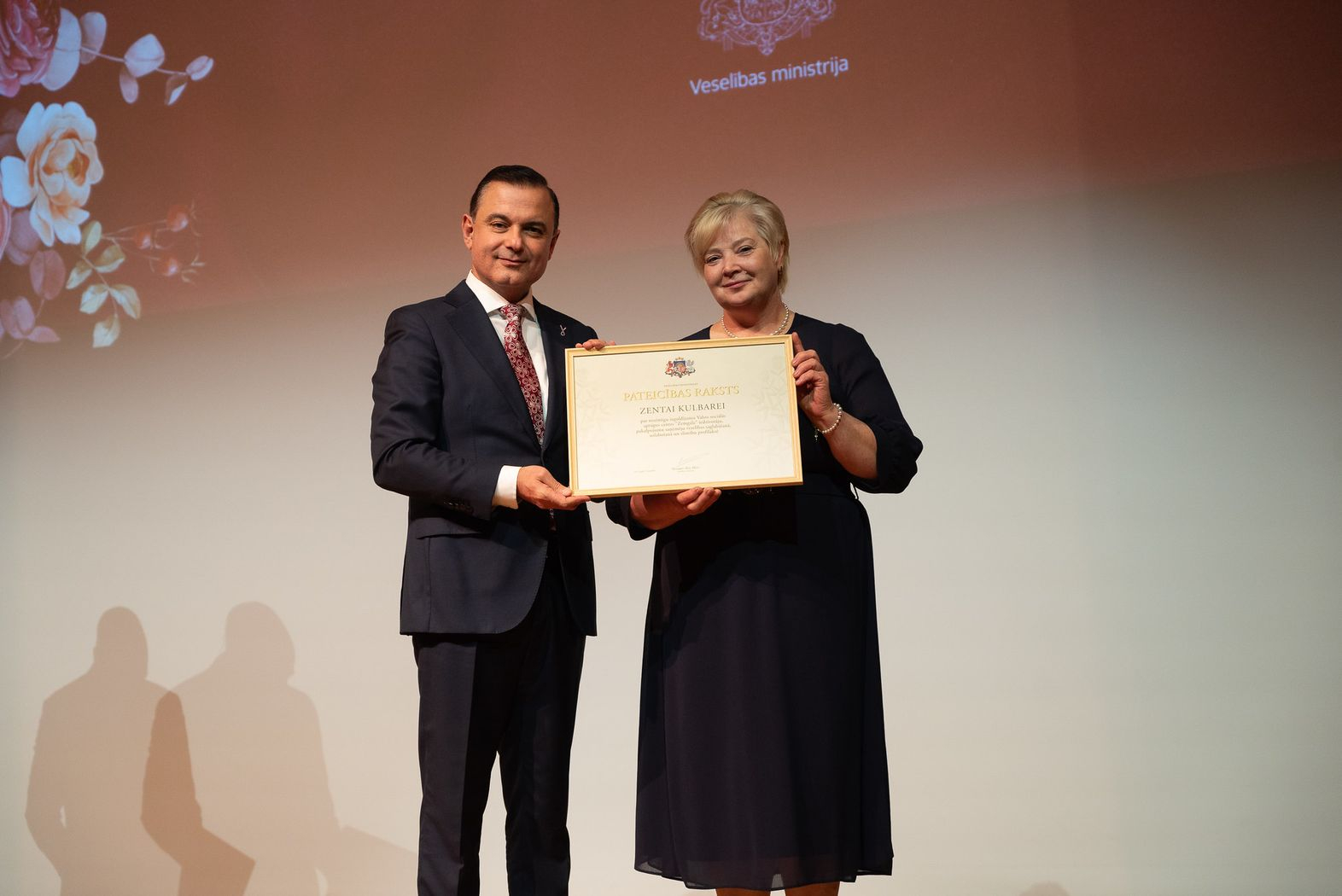 Attēlā veselības ministrs un vsac zemgale darbiniece ar saņemto apbalvojumu