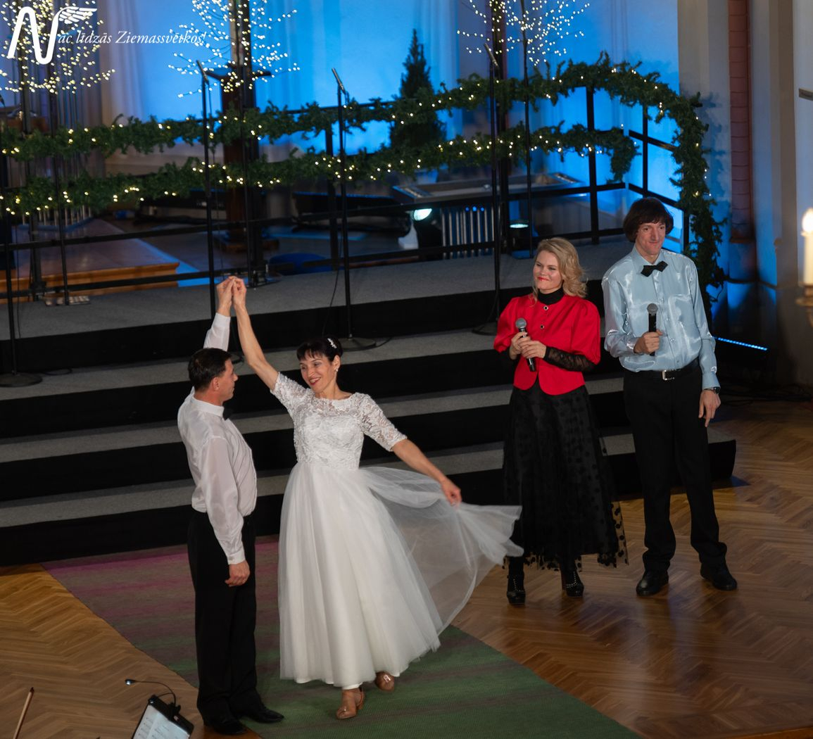 Pasākuma dalībnieki, dejotāji baltajos tērpos dejo pie dziesmas, kuru dzied divi solisti