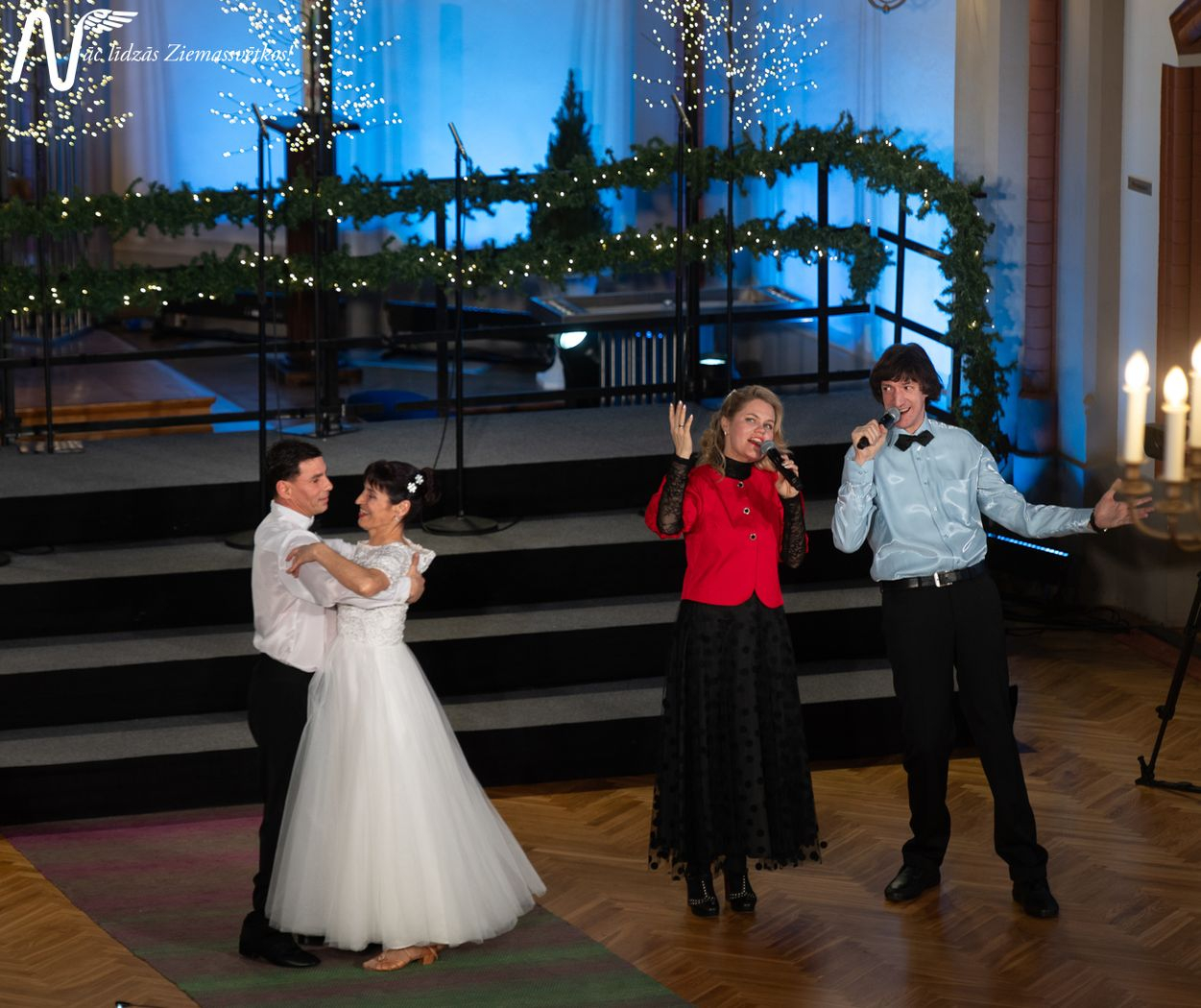 Pasākuma dalībnieki, dejotāji baltajos tērpos dejo pie dziesmas, kuru dzied divi solisti