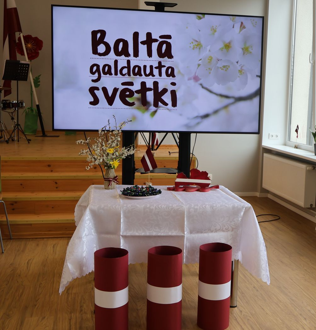 Uz galda balts galdauts un Latvijas dekorācijas