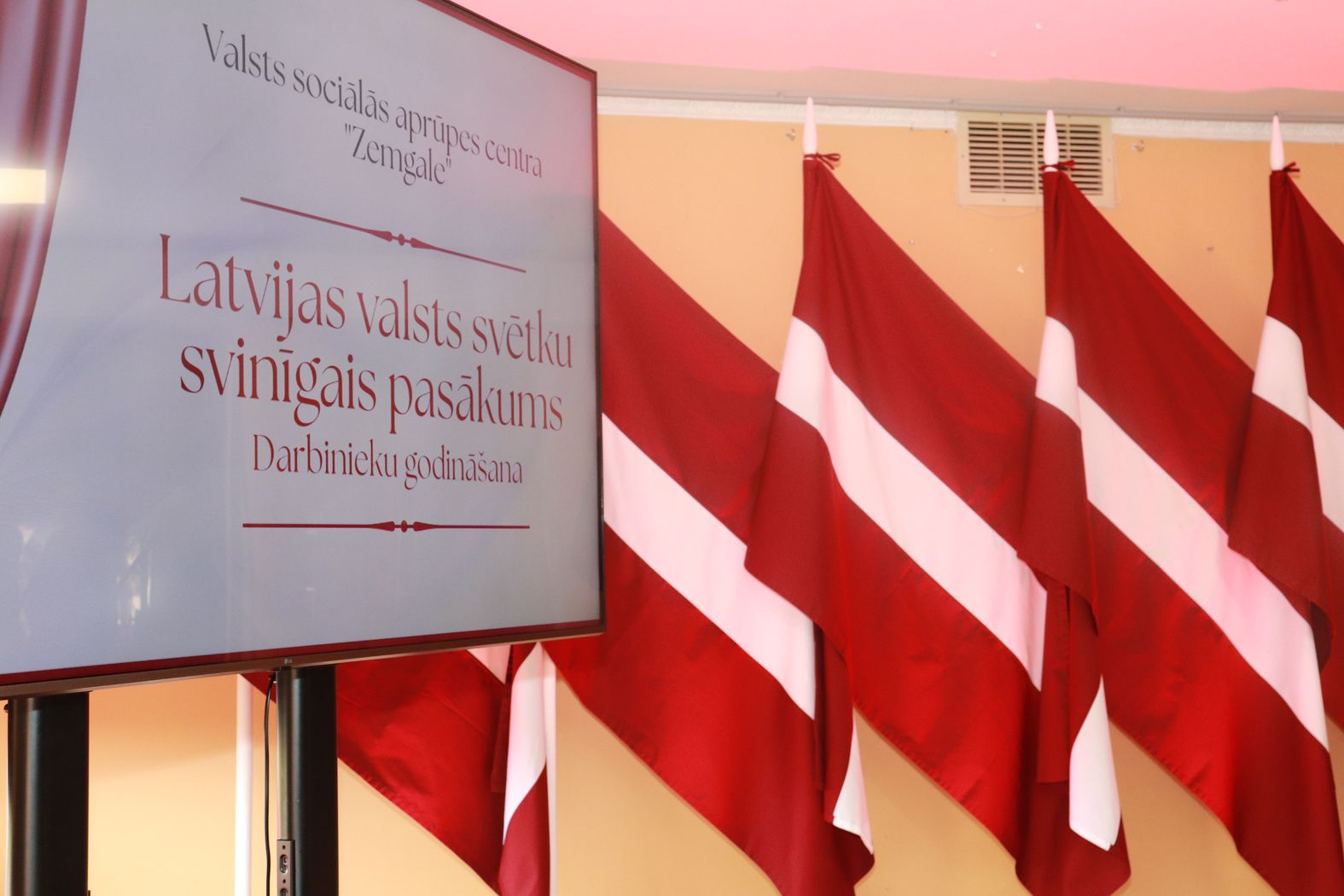 Pasākuma noformējums, ekrāns un fonā Latvijas karogi