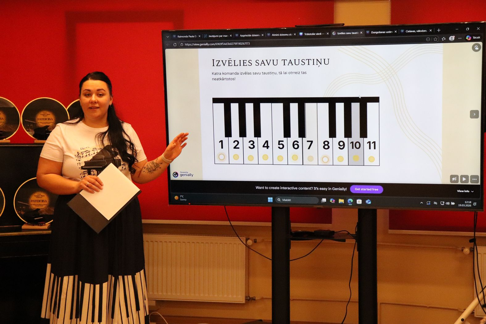 Pasākuma vadītāja pie ekrāna, kurā ir dziesmu minēšanas uzdevums