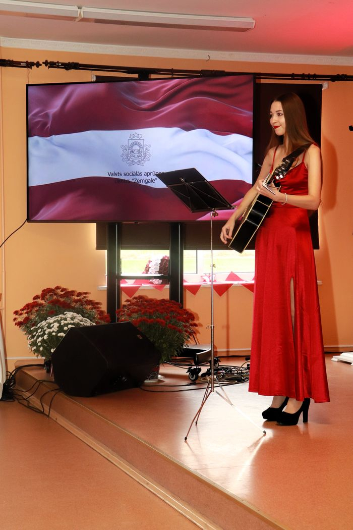 Dziedātāja Alise sarkanā garā kleitā ar ģitāru rokās