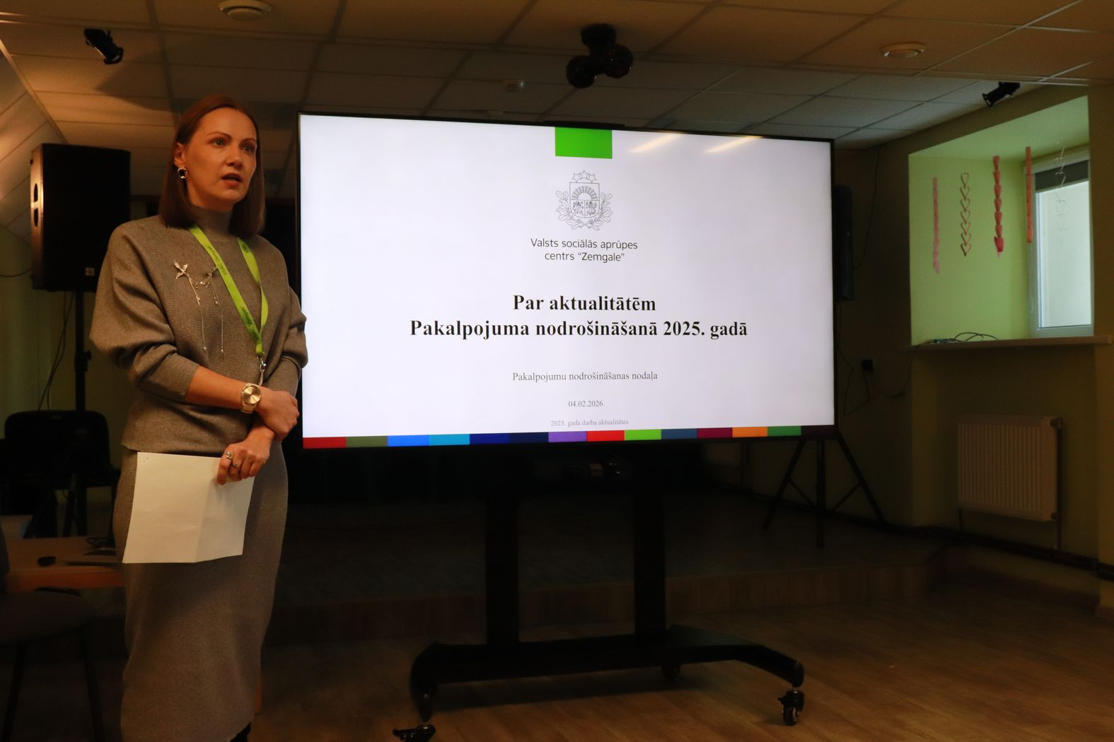 Lielais ekrāns ar prezentāciju un struktūrvienības vadītāja to prezentē