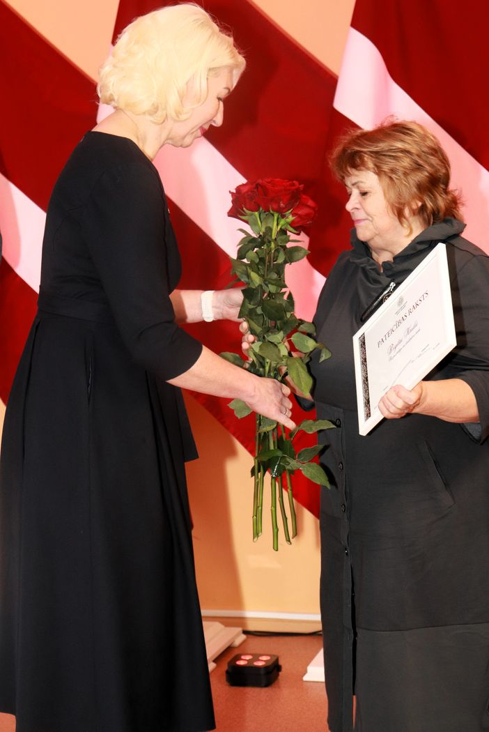 Apbalvojumu saņēmušais darbinieks bildē ar iestādes direktora vietnieci, kura pasniedz ziedus