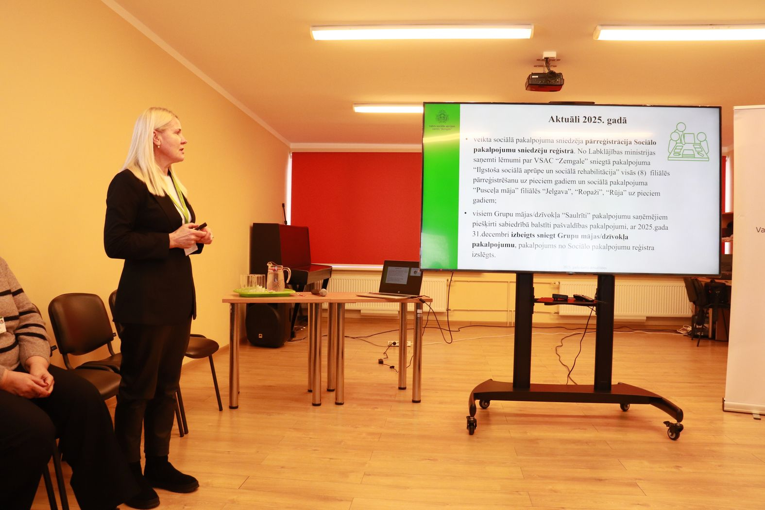 Lielais ekrāns ar prezentāciju un struktūrvienības vadītāja to prezentē