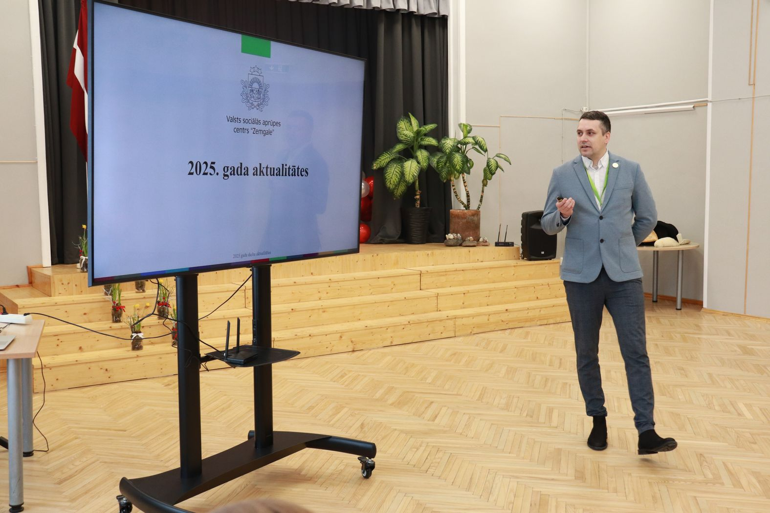 Lielais ekrāns ar prezentāciju un iestādes direktors to prezentē