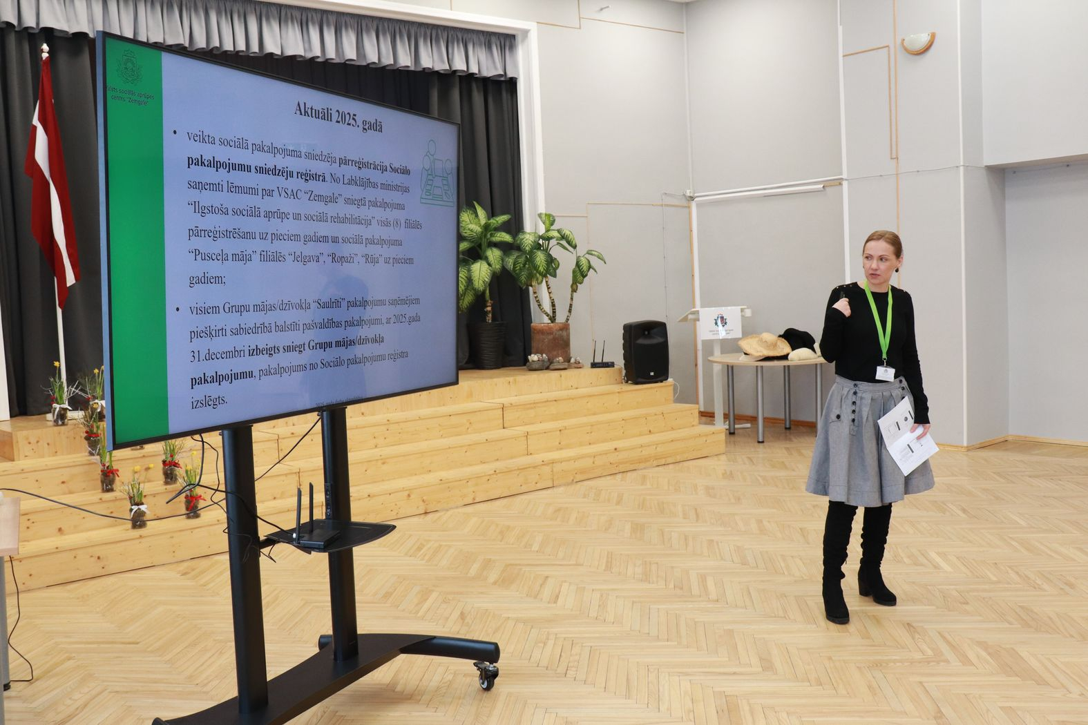 Lielais ekrāns ar prezentāciju un struktūrvienības vadītāja to prezentē