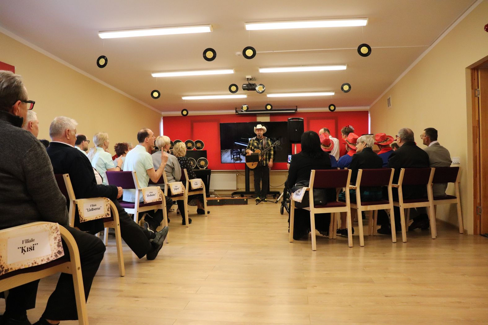 Pasākuma viesis dziedātājs Jānis Krūmiņš ar ģitāru un pilna zāle ar skatītājiem