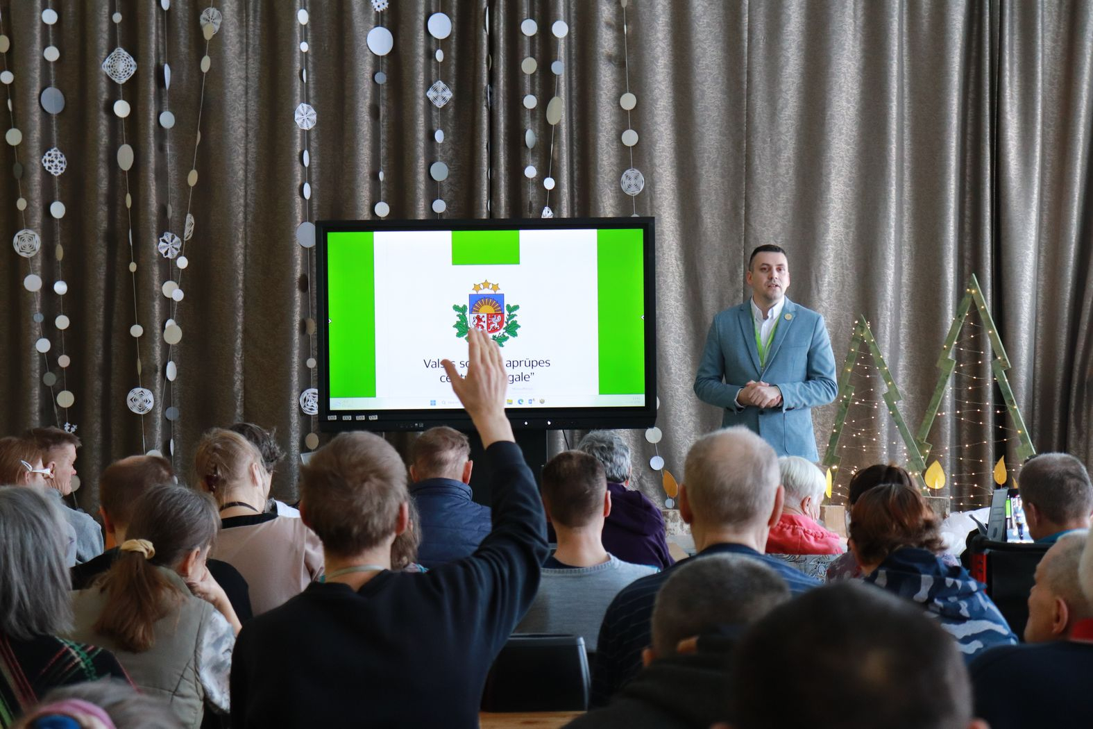 Zālē sēž iedzīvotāji, priekšā iestādes direktors vada kopsapulci