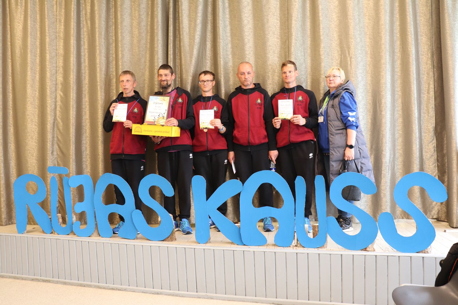 Komandas kopbilde ar diplomiem pie lielā uzraksta RŪJAS KAUSS