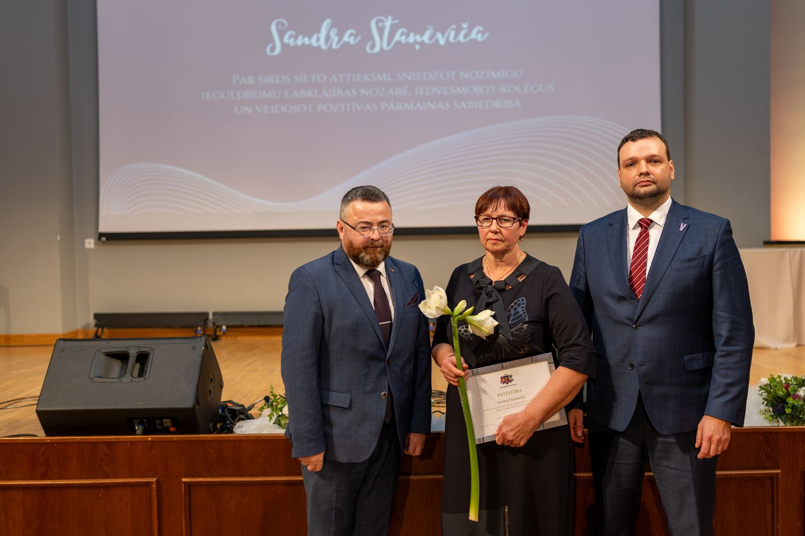 Apbalvojuma saņēmējs ar ziediem, pateicību kopbildē ar labklājības ministru un valsts sekretāru