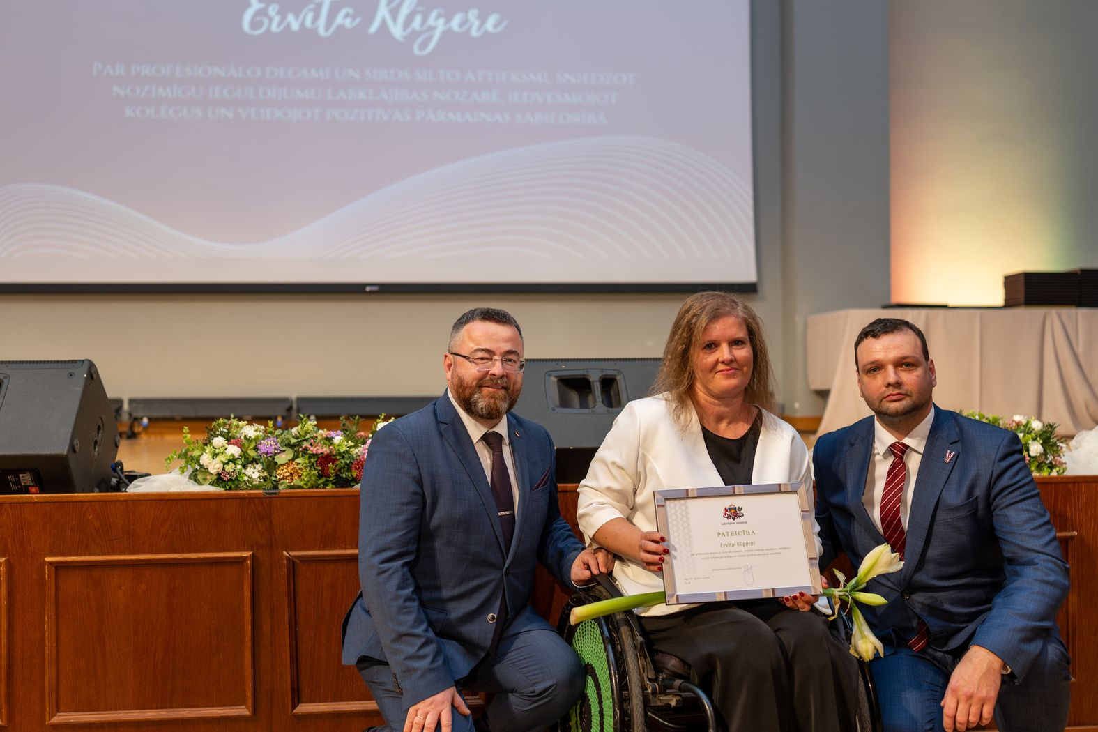 Apbalvojuma saņēmējs ar ziediem, pateicību kopbildē ar labklājības ministru un valsts sekretāru