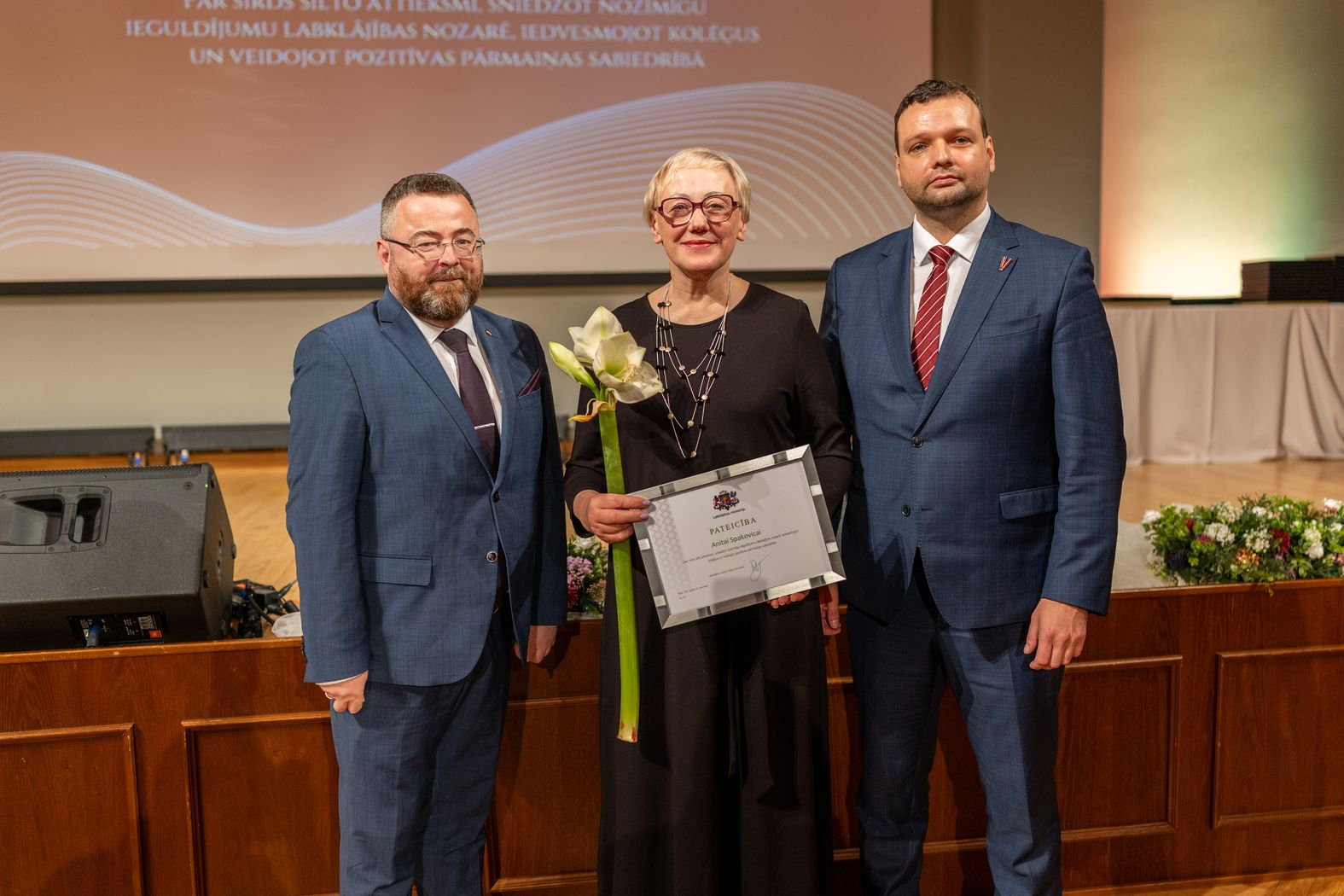 Apbalvojuma saņēmējs ar ziediem, pateicību kopbildē ar labklājības ministru un valsts sekretāru