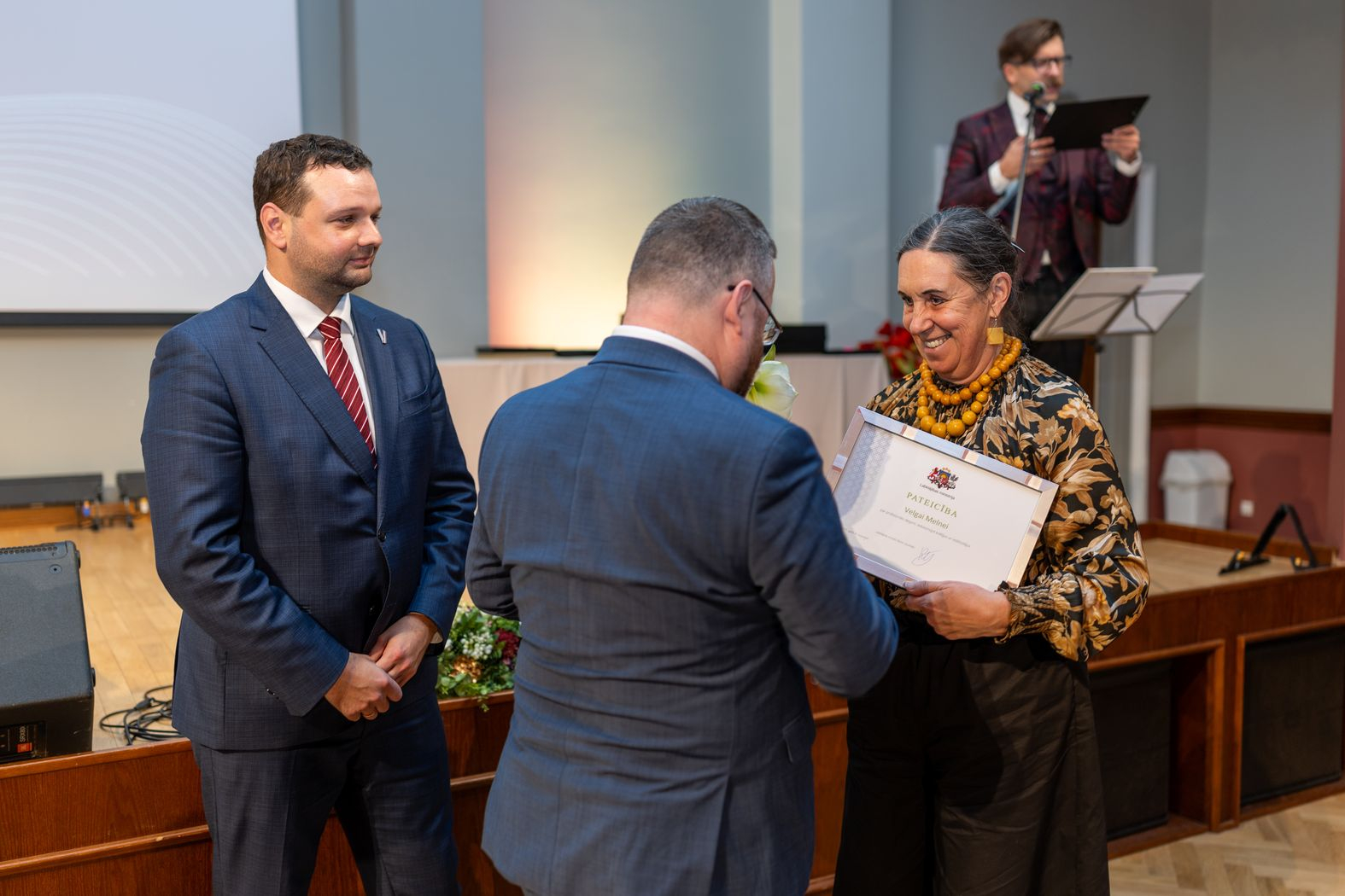 Apbalvojuma saņēmējs ar ziediem, pateicību kopbildē ar labklājības ministru un valsts sekretāru