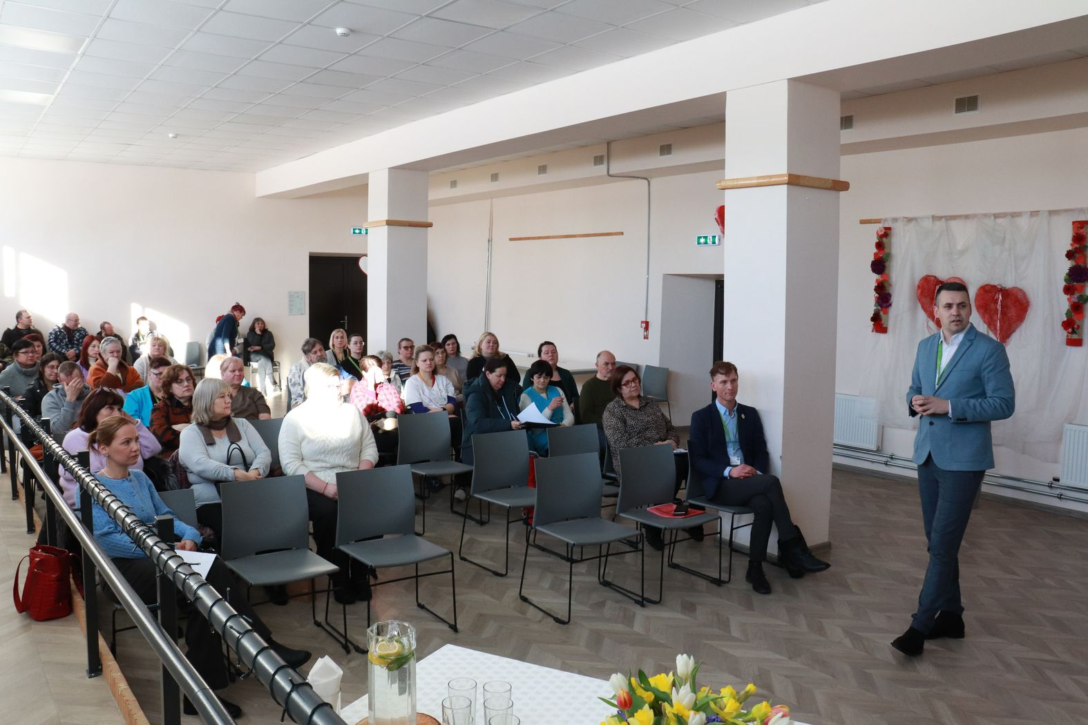 Zālē sēž darbinieki, priekšā direktors vada kopsapulci