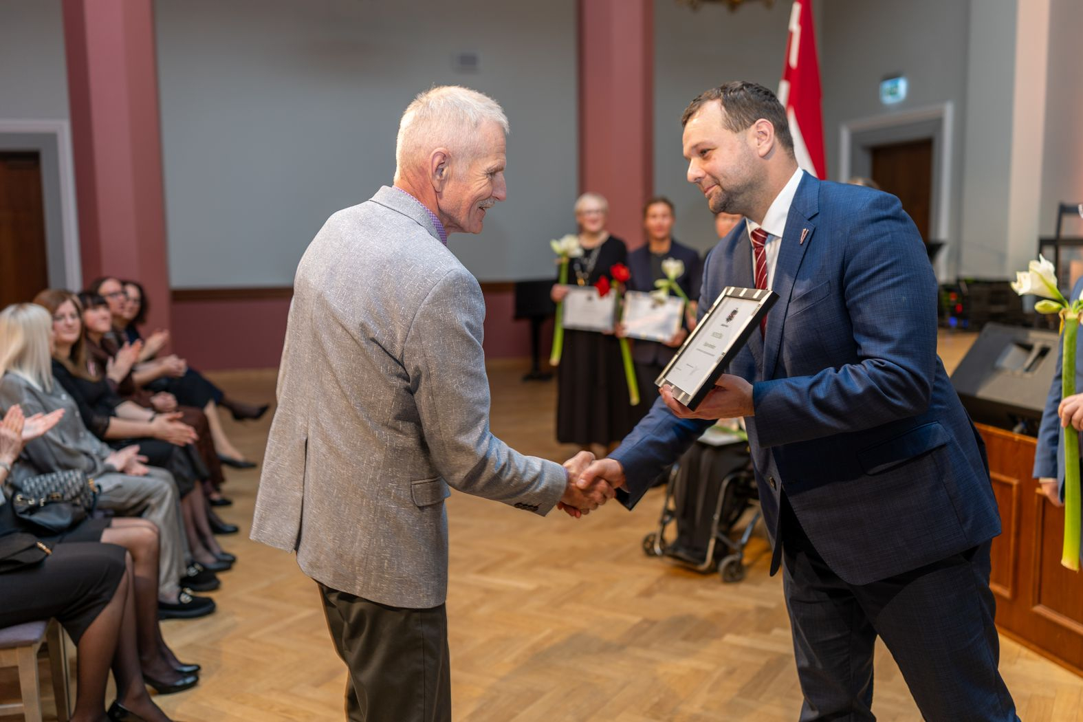 Apbalvojuma saņēmējs ar ziediem, pateicību kopbildē ar labklājības ministru 