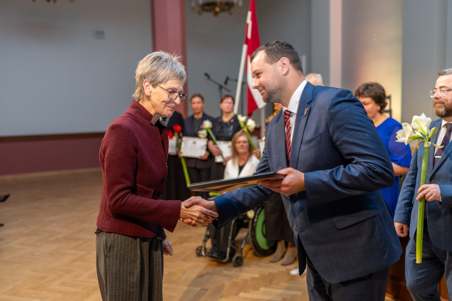 Apbalvojuma saņēmējs ar ziediem, pateicību kopbildē ar labklājības ministru 