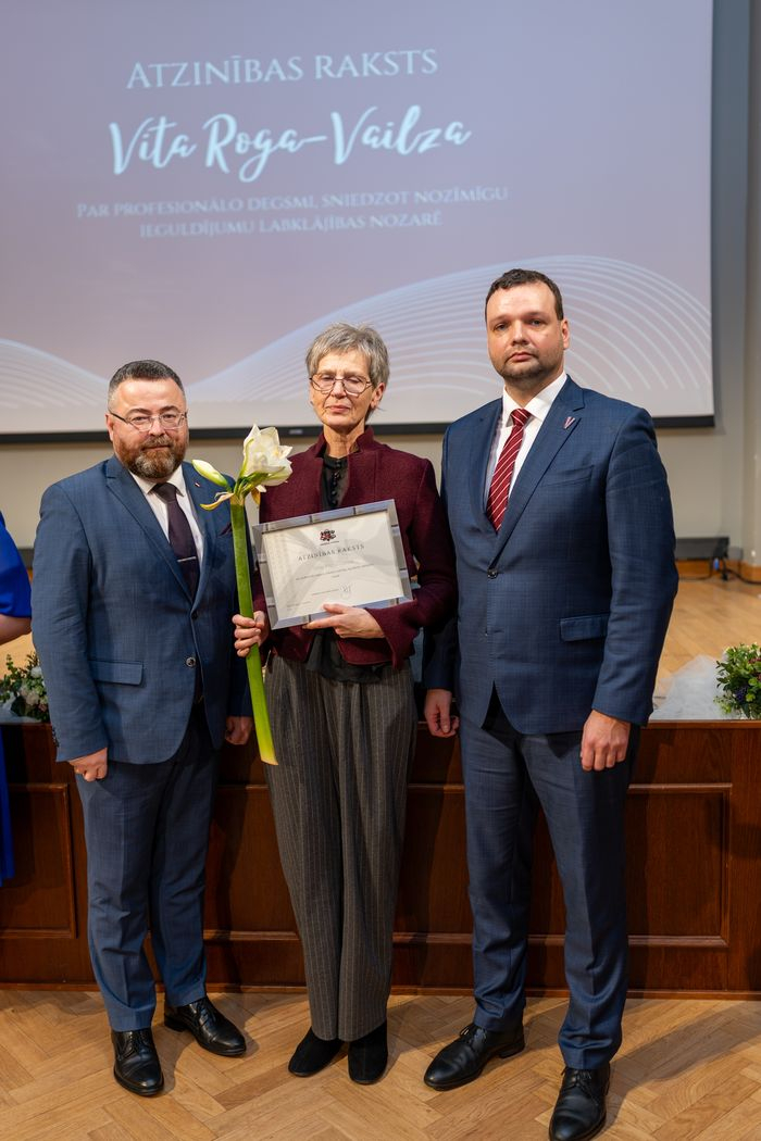 Apbalvojuma saņēmējs ar ziediem, pateicību kopbildē ar labklājības ministru un valsts sekretāru