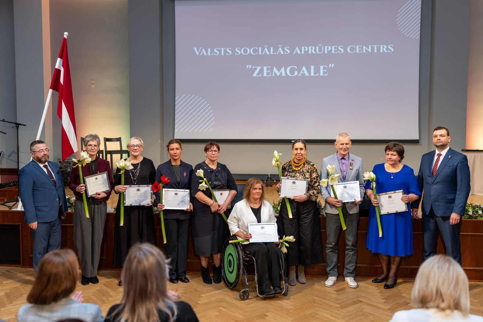 Apbalvojuma saņēmēji ar ziediem, pateicībām kopbildē ar labklājības ministru un valsts sekretāru