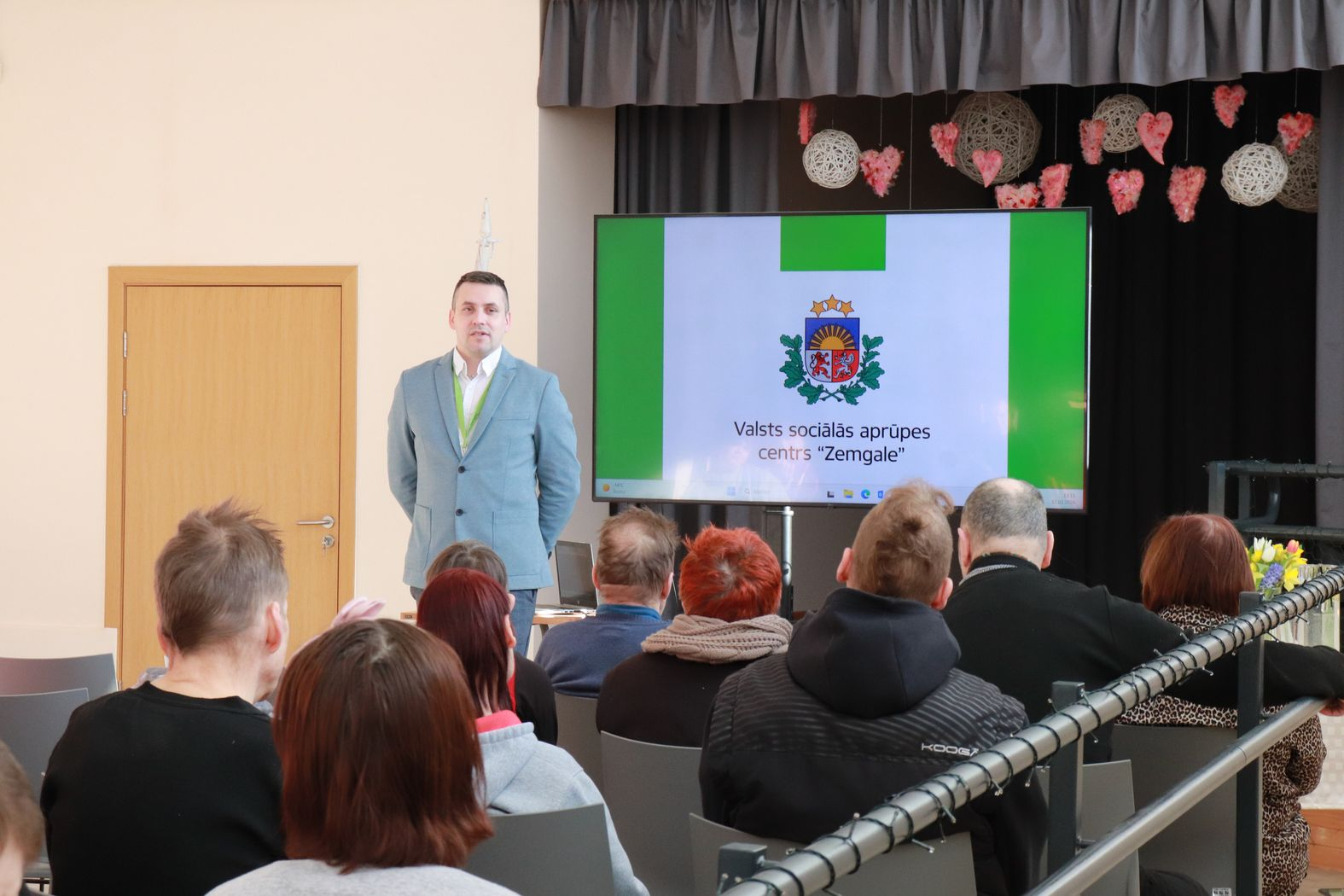 Zālē sēž iestādes iedzīvotāji, priekšā iestādes direktors vada kopsapulci