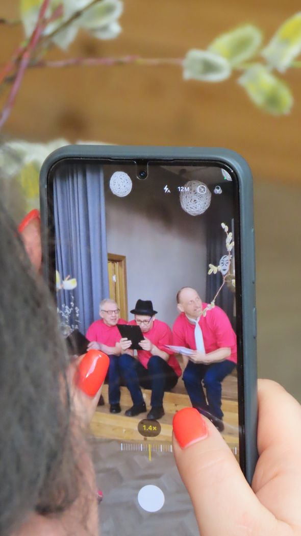 Caur telefonu bildē uz skatuves esošos trīs pasākuma dalībniekus