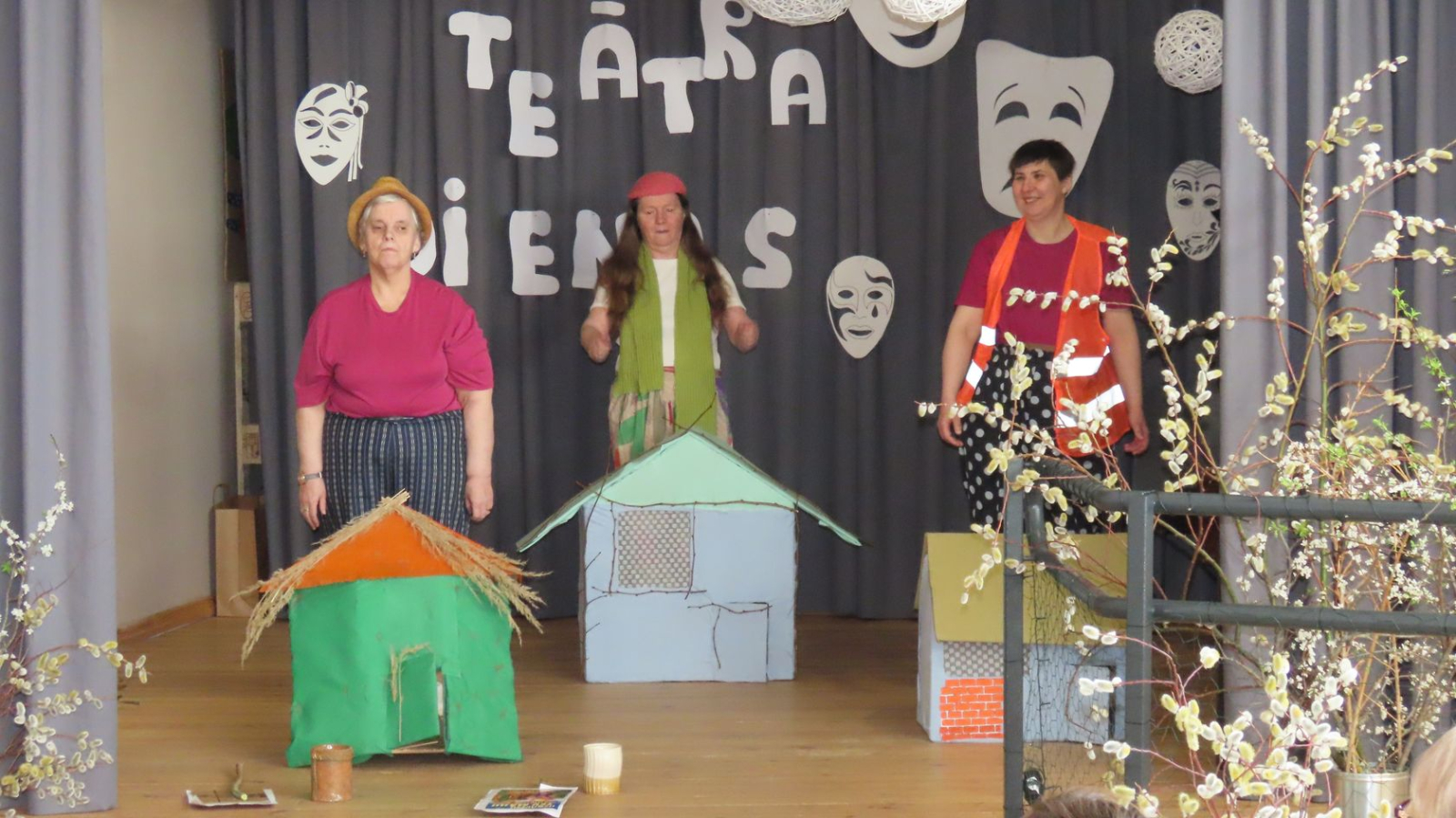 Uzstājas dalībnieki, trīs sivēni pie kartona mājām