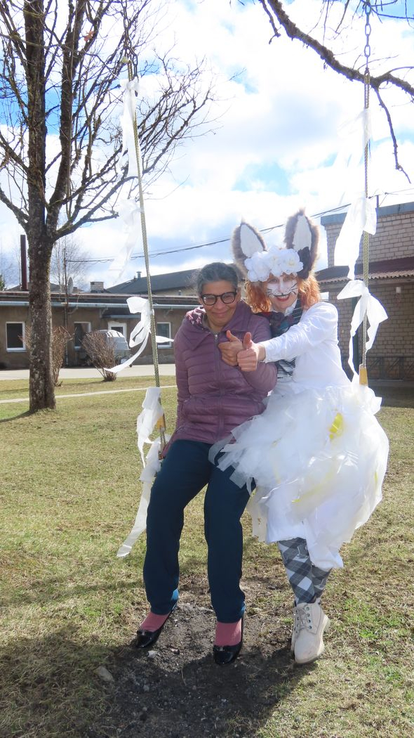 Divi cilvēki ārā uz šūpolēm. Viens ir ģērbies kā zaķis