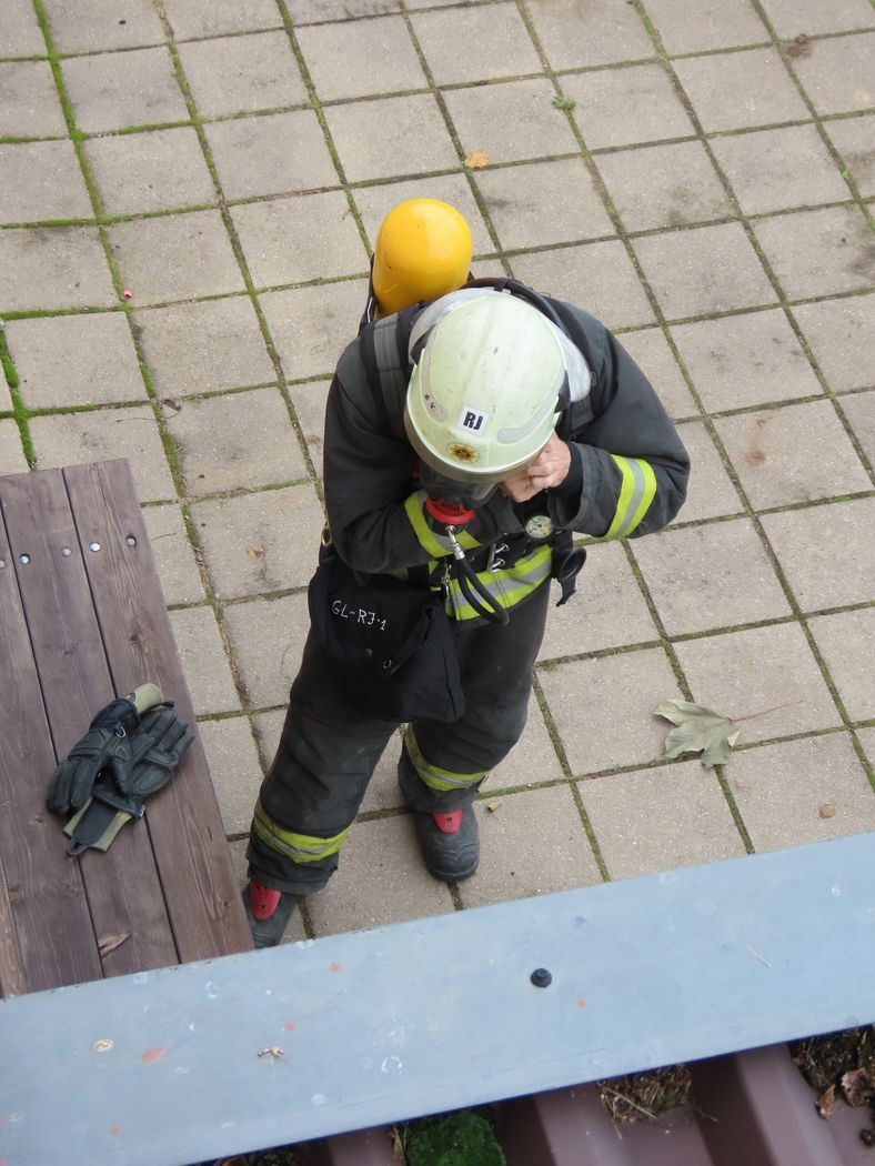 Attēlā ugunsdzēsējs, kurš gatavojas ieiet piedūmotā ēkā