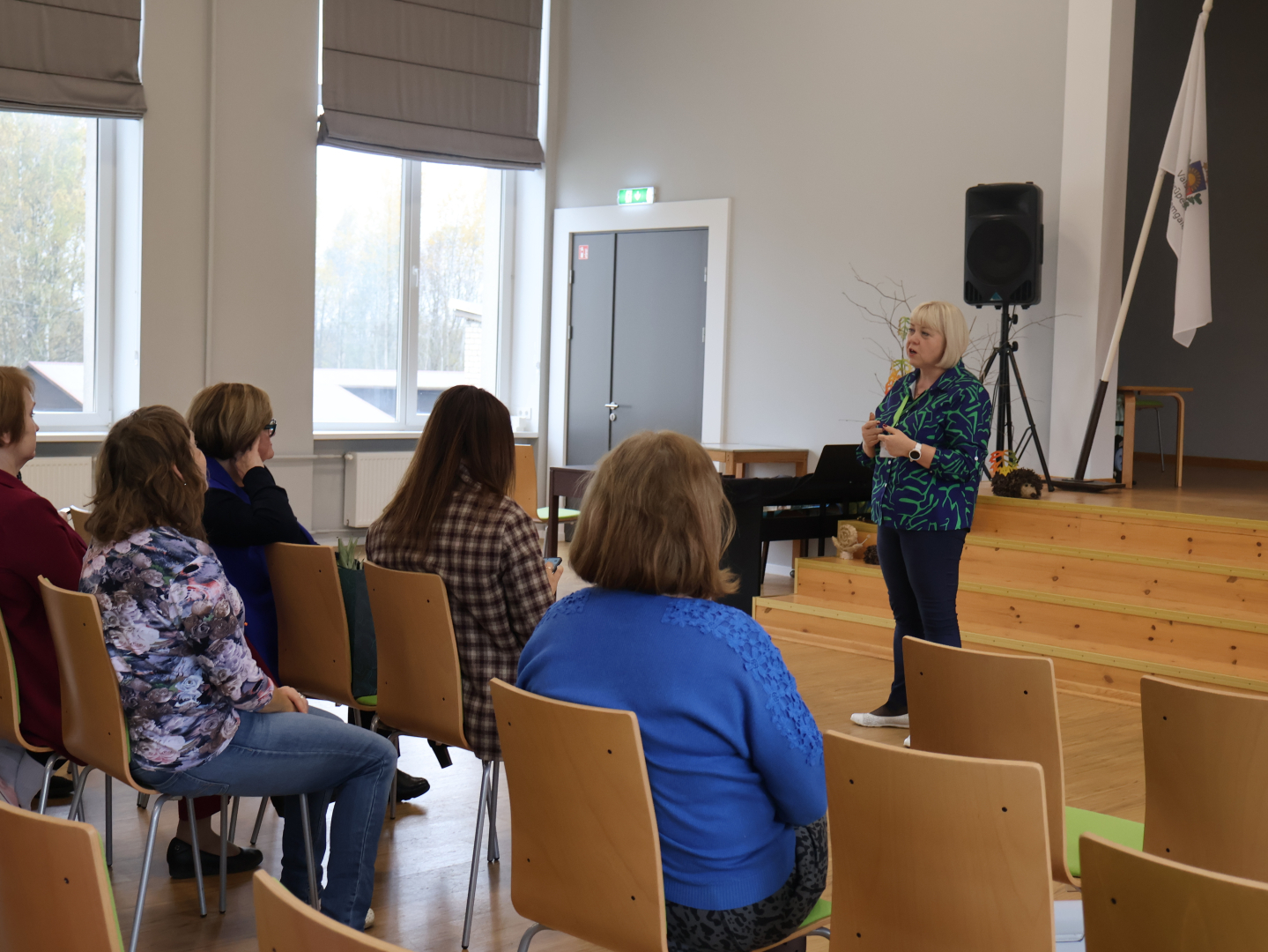 Zāles priekšā runā mākslas terapeite. Zālē sēž klausītāji